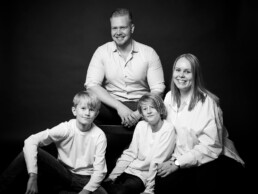 Familie fotograferet i studie på hvid baggrund. Klassisk familieportræt i sort hvid. Familiefotografering til private.
